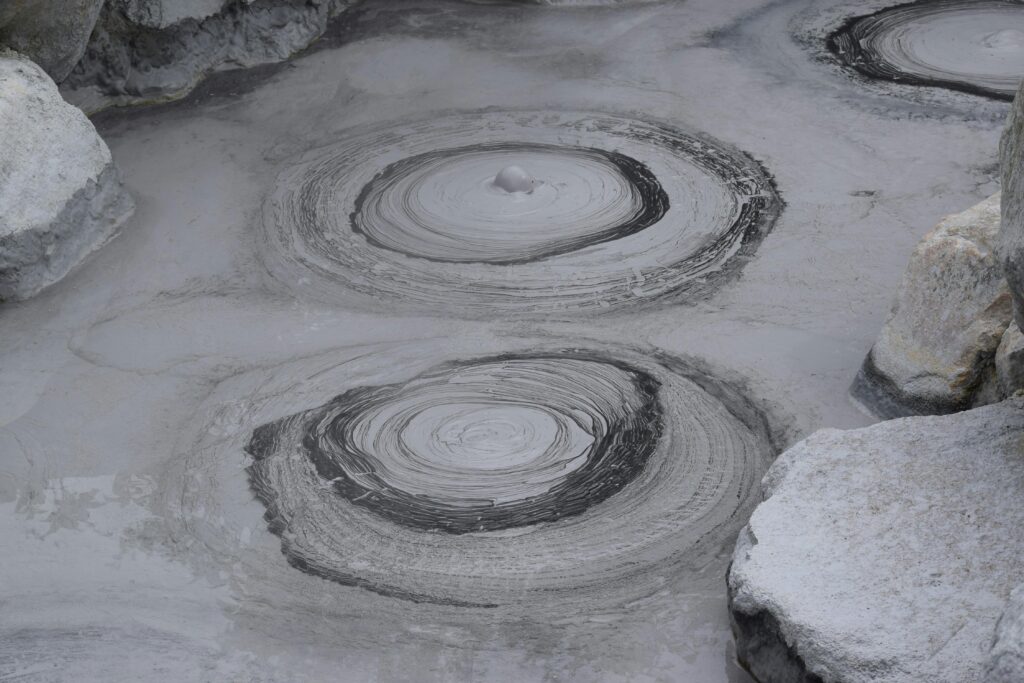 Gray geothermal mud pools with bubbling patterns in Beppu, Japan.