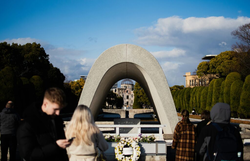Visitors at Hiroshima Peace Memorial Park with cenotaph arch framing the Atomic Bomb Dome in the background.