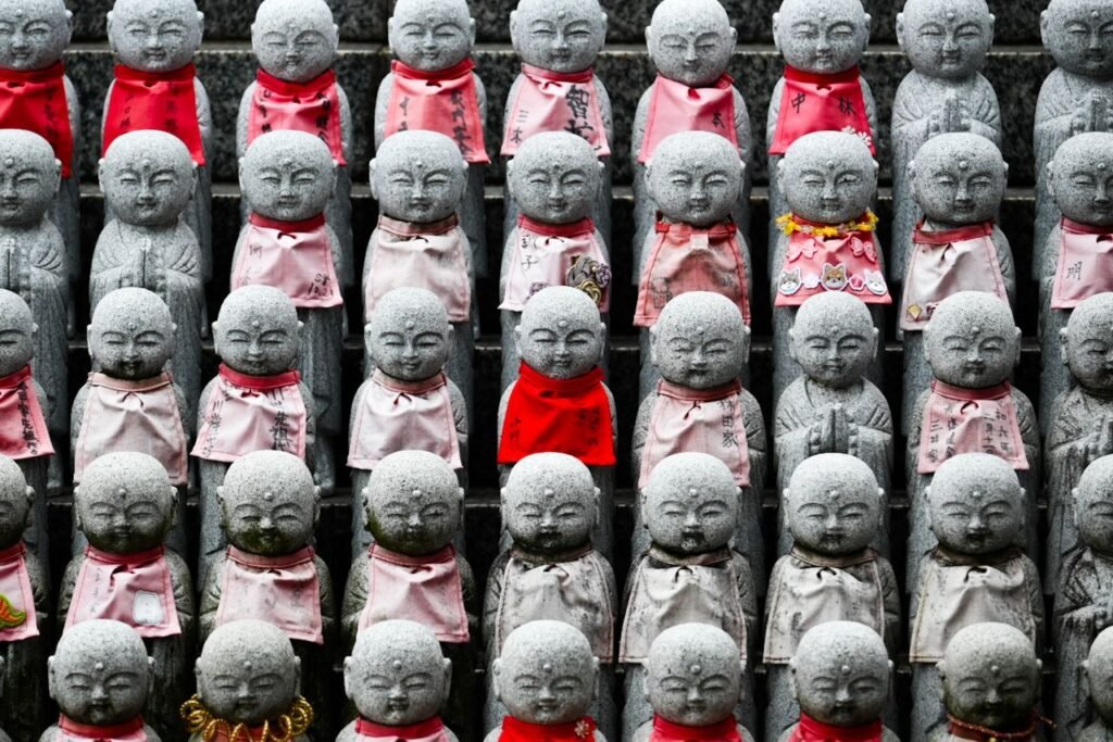 Multiple stone Jizo statues wearing red and pink bibs, symbolizing protection, in Osaka, Japan.